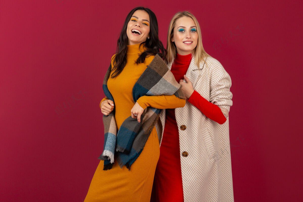 冷两位笑容可掬的时尚女性穿着秋冬时装和外套 在红墙上孤零零地摆着姿势时尚外套姿势