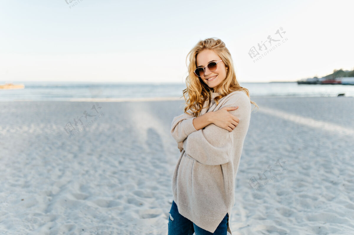 配件穿着大号毛衣和牛仔裤的女人在海边摆出很好的姿势金发活跃活动