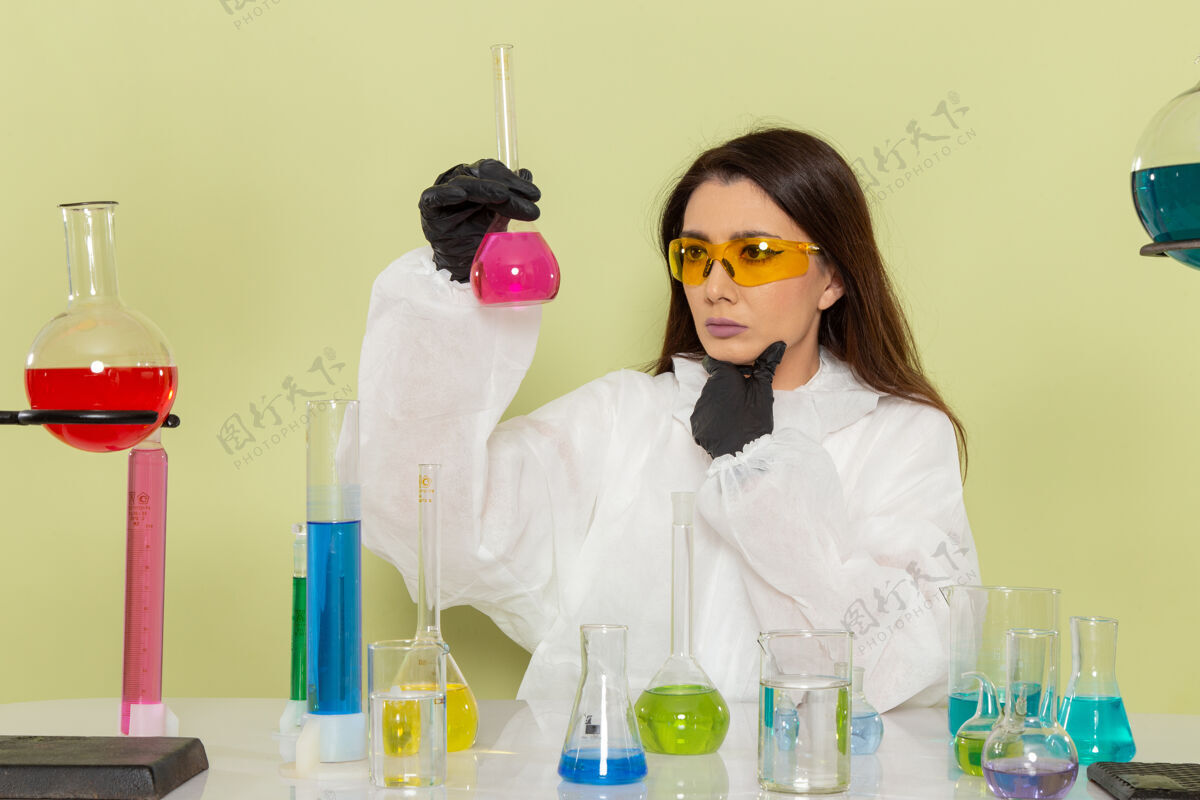 工作正面图身着特殊防护服的女化学家在绿色办公桌上思考解决方案化学外套化学
