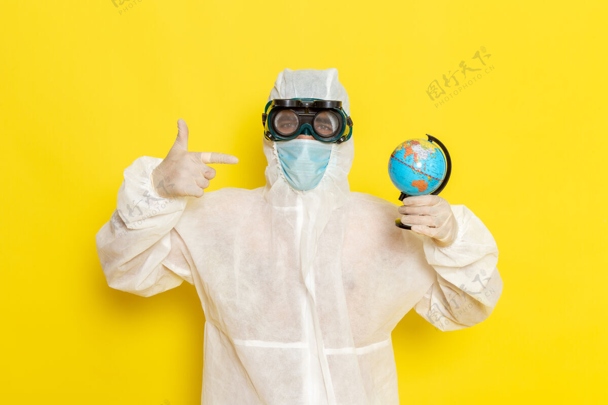特殊正面图：身着特殊套装的男科学工作者手持小圆球 在黄色的办公桌上摆姿势地球仪圆桌子
