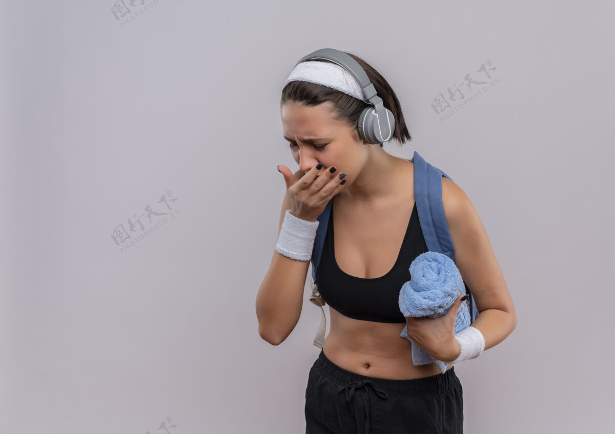 运动穿着运动服 背着背包 头上戴着耳机 拿着毛巾 站在白墙上咳嗽 看起来很不舒服年轻人女性人
