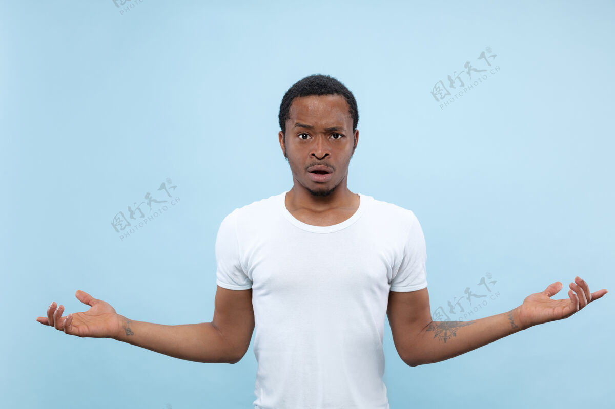 肖像半身特写 蓝色背景 身穿白衬衫的非洲裔美国青年人类情感 面部表情 广告概念询问和不确定 怀疑 负面情绪商人年轻面部