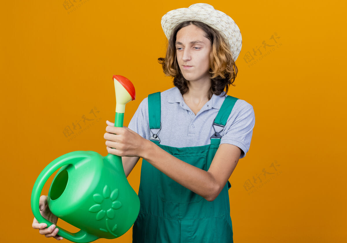 花园年轻的园丁穿着连体衣戴着帽子拿着浇水罐穿浇水年轻