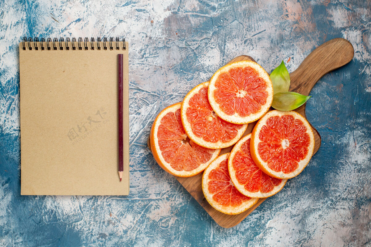 视图俯视图在砧板上切葡萄柚笔记本和蓝白表面上的铅笔切的铅笔切的葡萄柚