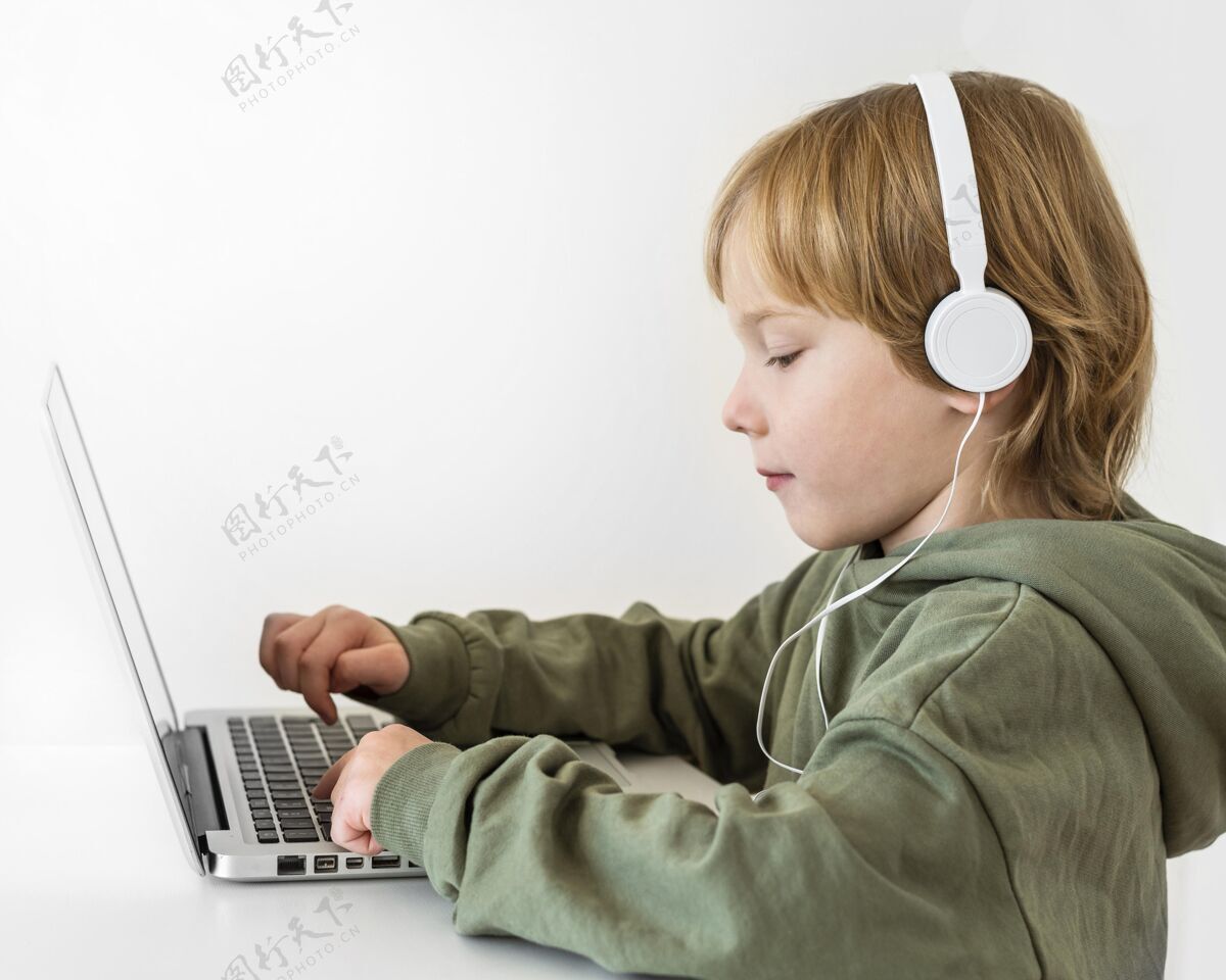 消遣小男孩使用带耳机的笔记本电脑的侧视图年轻人娱乐孩子