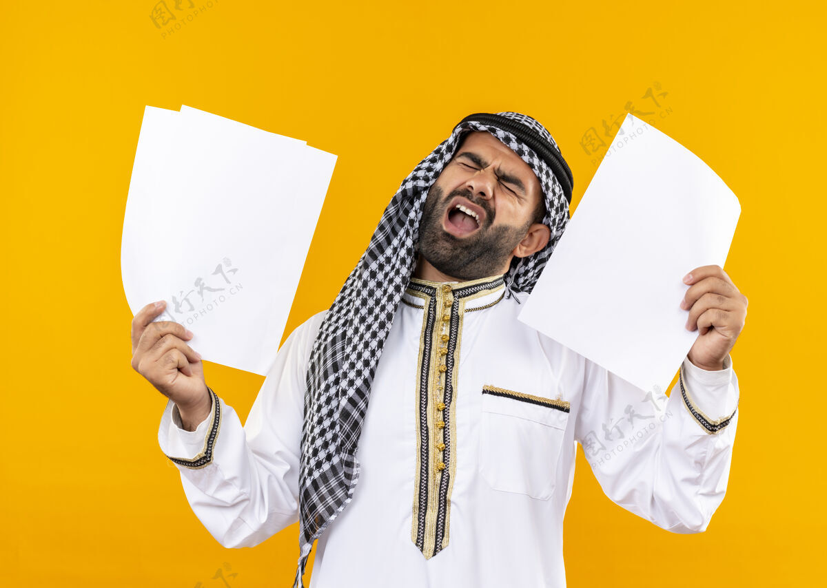 阿拉伯语身着传统服装的阿拉伯商人站在橙色的墙上 手里拿着空白页 带着恼怒的表情大喊大叫传统空白表达