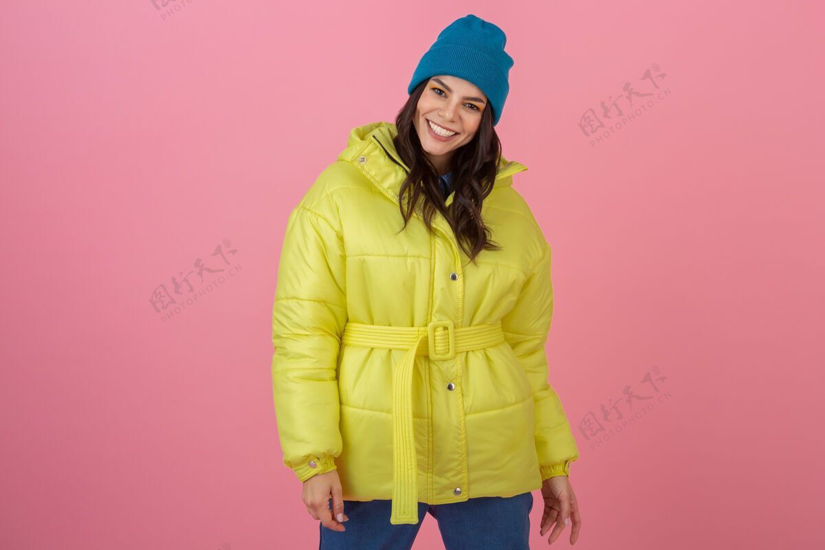 夹克迷人活跃的女人穿着鲜艳的黄色冬季羽绒服在粉色墙壁上摆造型 笑容可掬 温暖的外套时尚潮流 疯狂惊艳的表情快乐运动装滑雪板