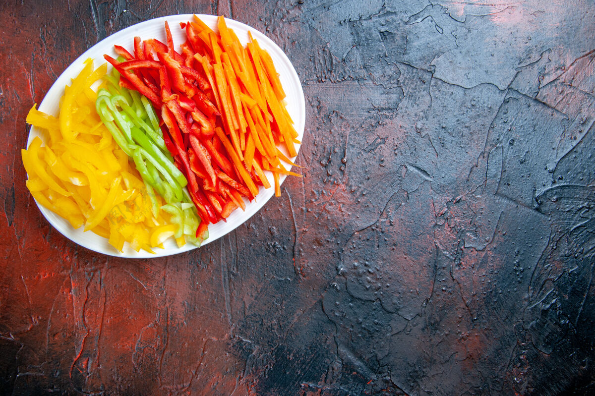 盘子顶视图彩色切辣椒在白色盘子上暗红色的桌子与自由的地方胡椒景观晚餐