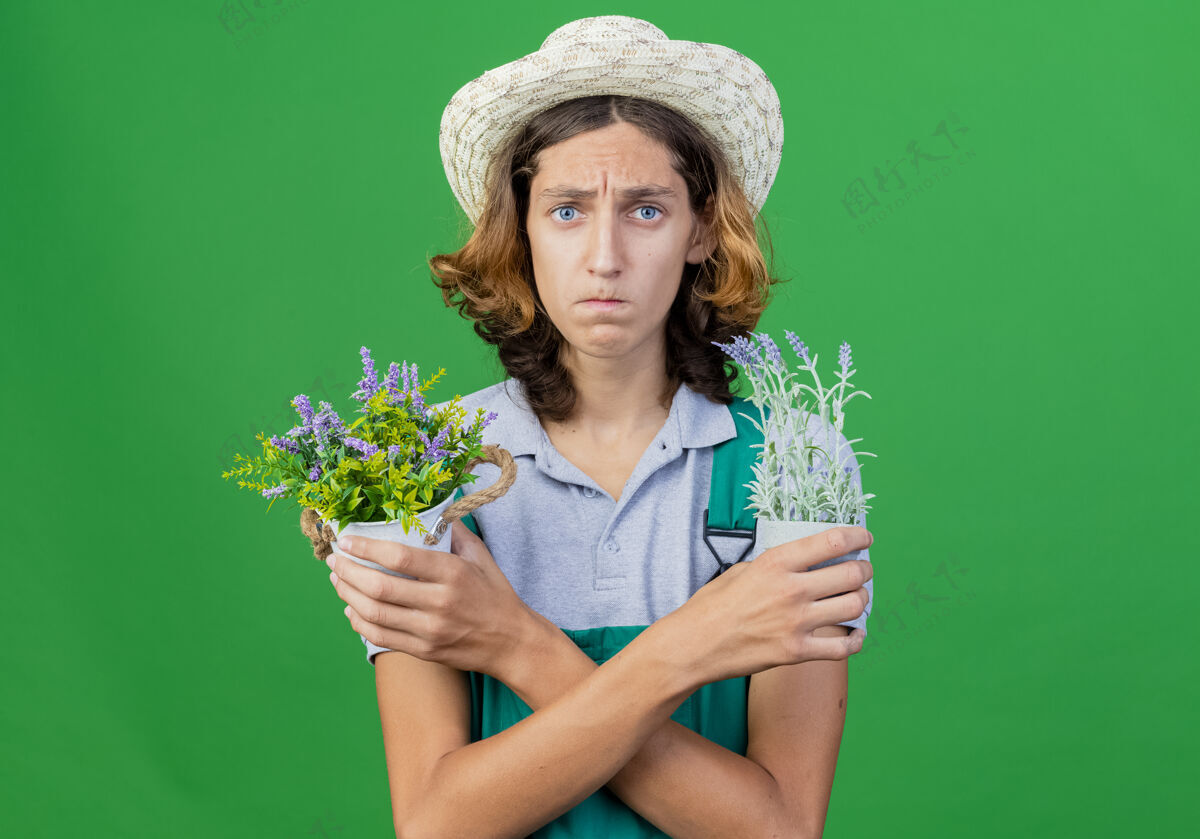 连身衣年轻的园丁 穿着连体衣 戴着帽子 手里拿着盆栽植物 表情悲伤植物年轻帽子