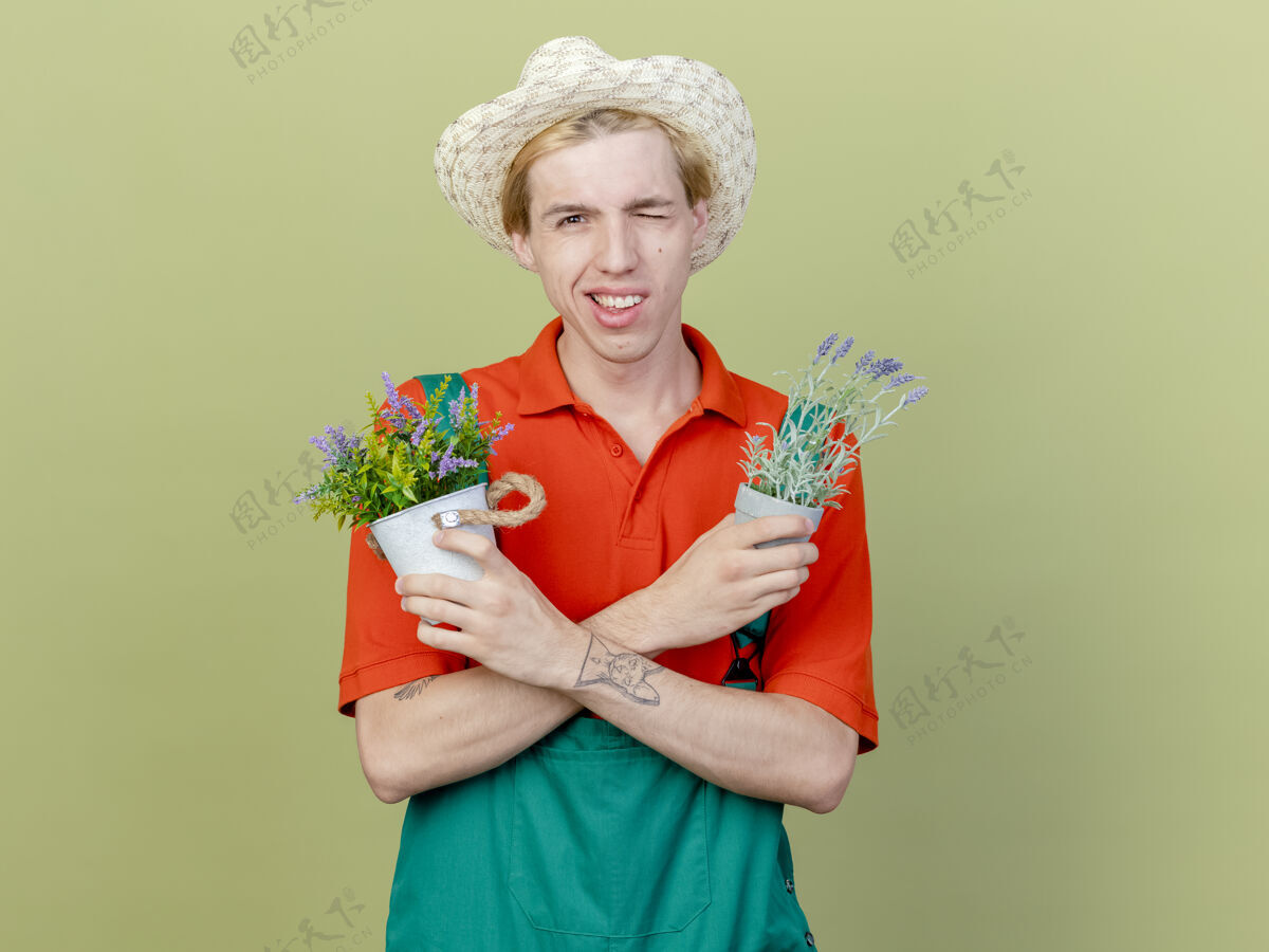 穿着年轻的园丁 穿着连体衣 戴着帽子 手里拿着盆栽植物眨眼男人植物