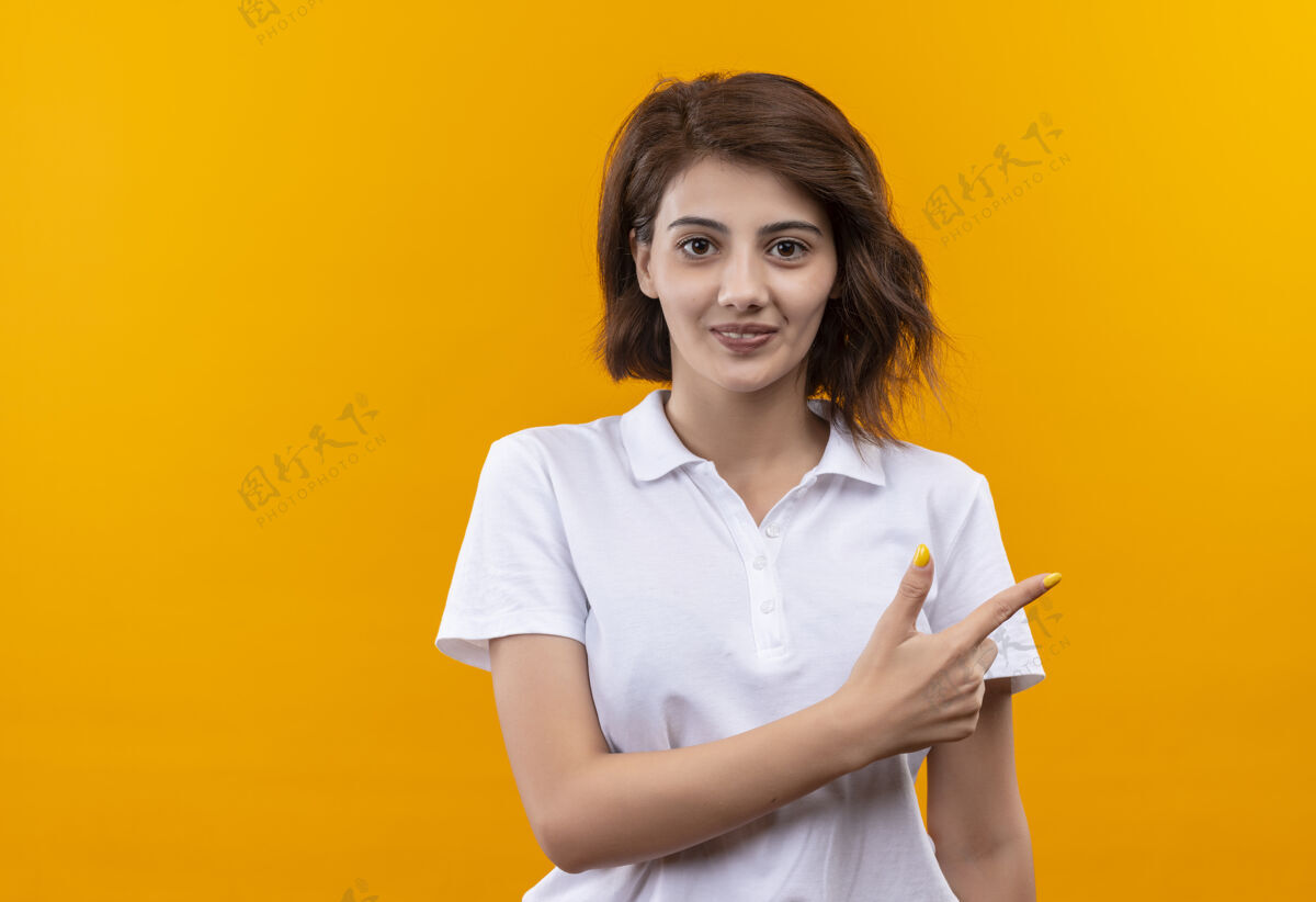 年轻短发女孩穿着白色马球衫 用食指指着侧面 看起来很自信橙色目录短裤