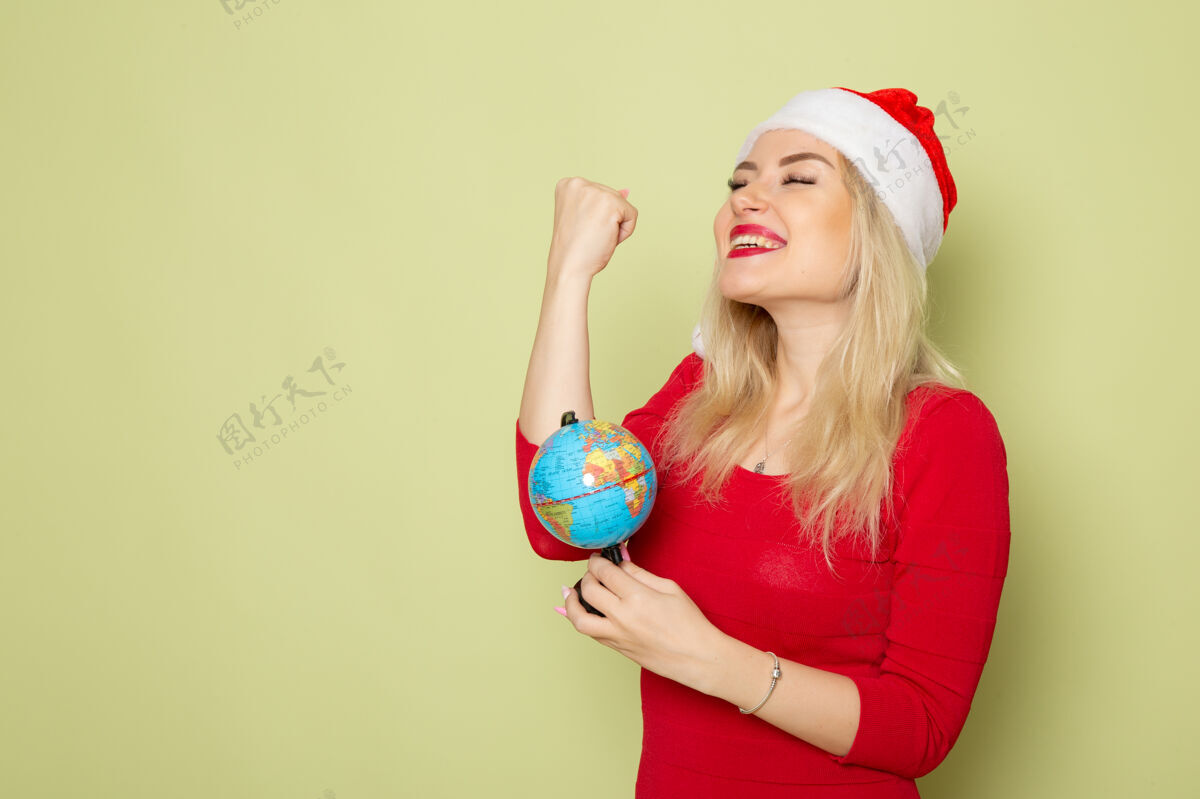 漂亮正面图漂亮的女人拿着地球仪在绿色的墙上假日圣诞节雪新年情感色彩金发漂亮的女人情感