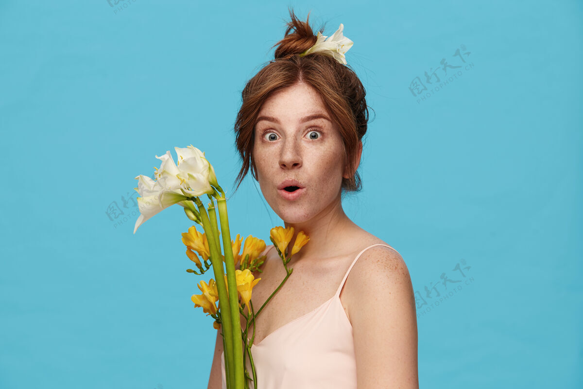 惊人一张室内照片 年轻激动的红发女士惊奇地围着绿色的眼睛看着相机 手里拿着一束鲜花 站在蓝色的背景上皮带站立黄色