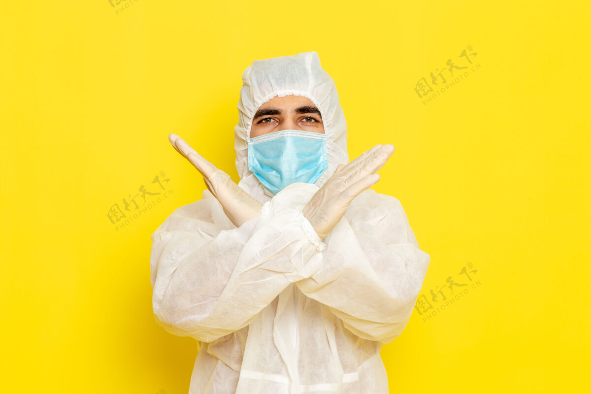 工人身穿白色特殊防护服 戴着黄色墙壁上显示禁止标志的面罩的男性科学工作者的正面图科学套装化学