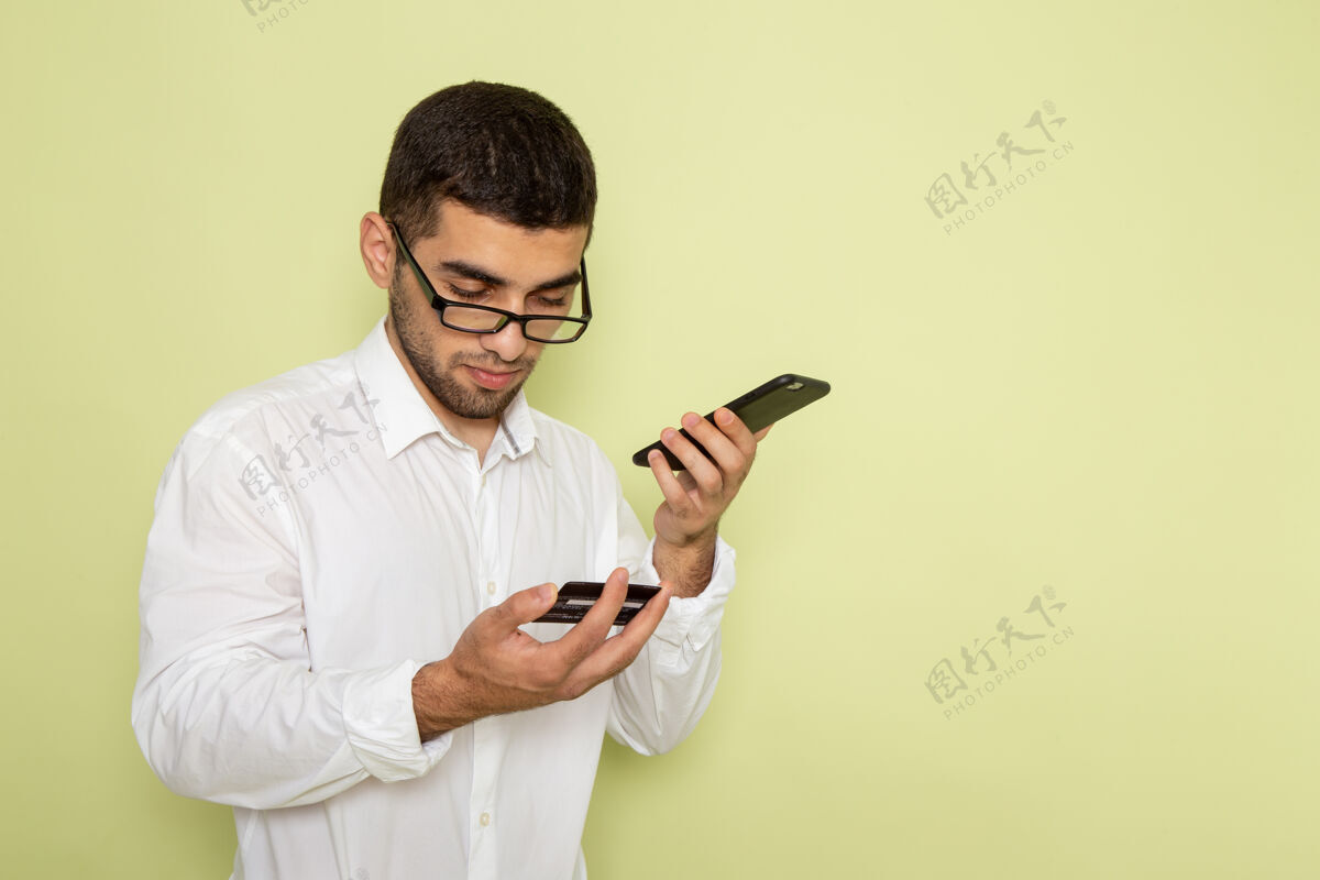 服装身穿白衬衫的男性上班族在浅绿色墙上手持并使用手机的前视图实验室外套工作男人