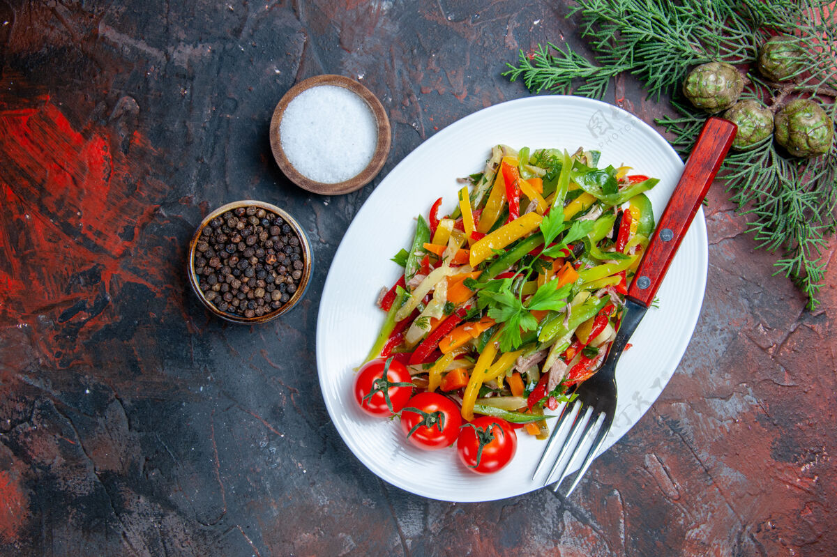 蔬菜沙拉俯瞰蔬菜沙拉叉在椭圆形盘子上不同的香料在小碗里在深红色的桌子上盘子辣椒深色