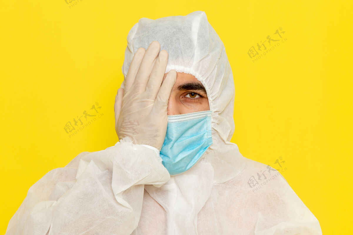 面部身穿白色特殊防护服的男性科学工作者的正面图 黄色墙壁上的半张脸上覆盖着无菌口罩科学工人男性