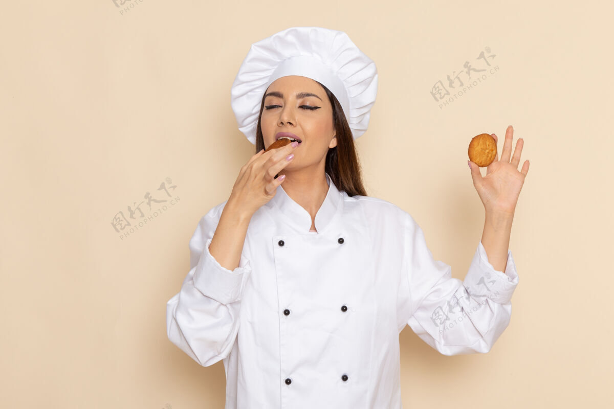 烹饪身穿白色厨师服的年轻女厨师在白墙上吃饼干的正面图套装饼干女性