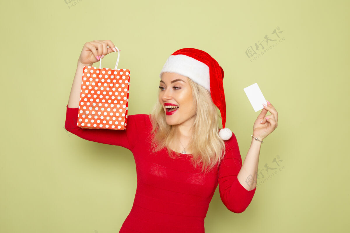 银行正面风景美丽的女人拿着礼物在小包装和银行卡上的绿色墙壁雪情感节日圣诞新年的颜色小雪漂亮的女人