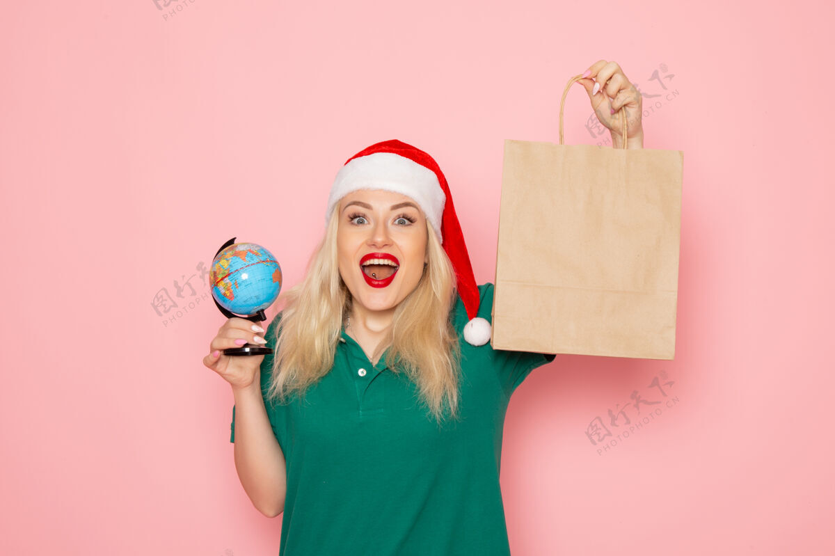 女人正面图年轻女性手持地球仪和圣诞礼物在粉色墙壁上模特女性圣诞节新年假期喜剧演员年轻女性成人