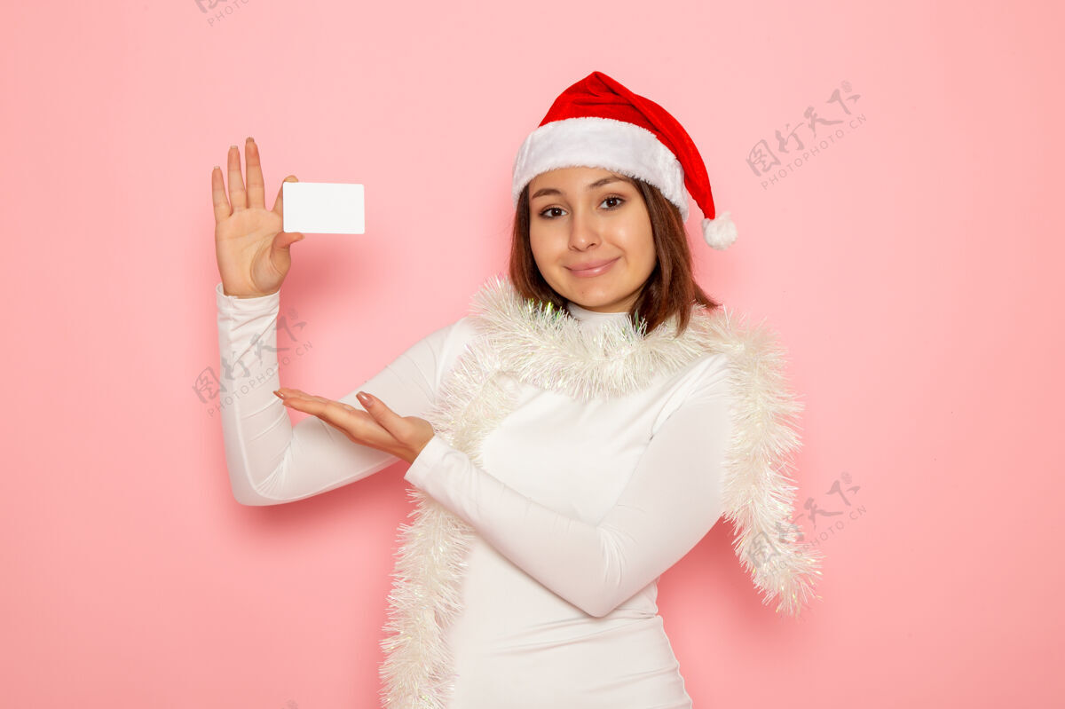 圣诞节正面图年轻女性手持白色银行卡在粉色墙上新年时尚彩钱度假漂亮风景银行