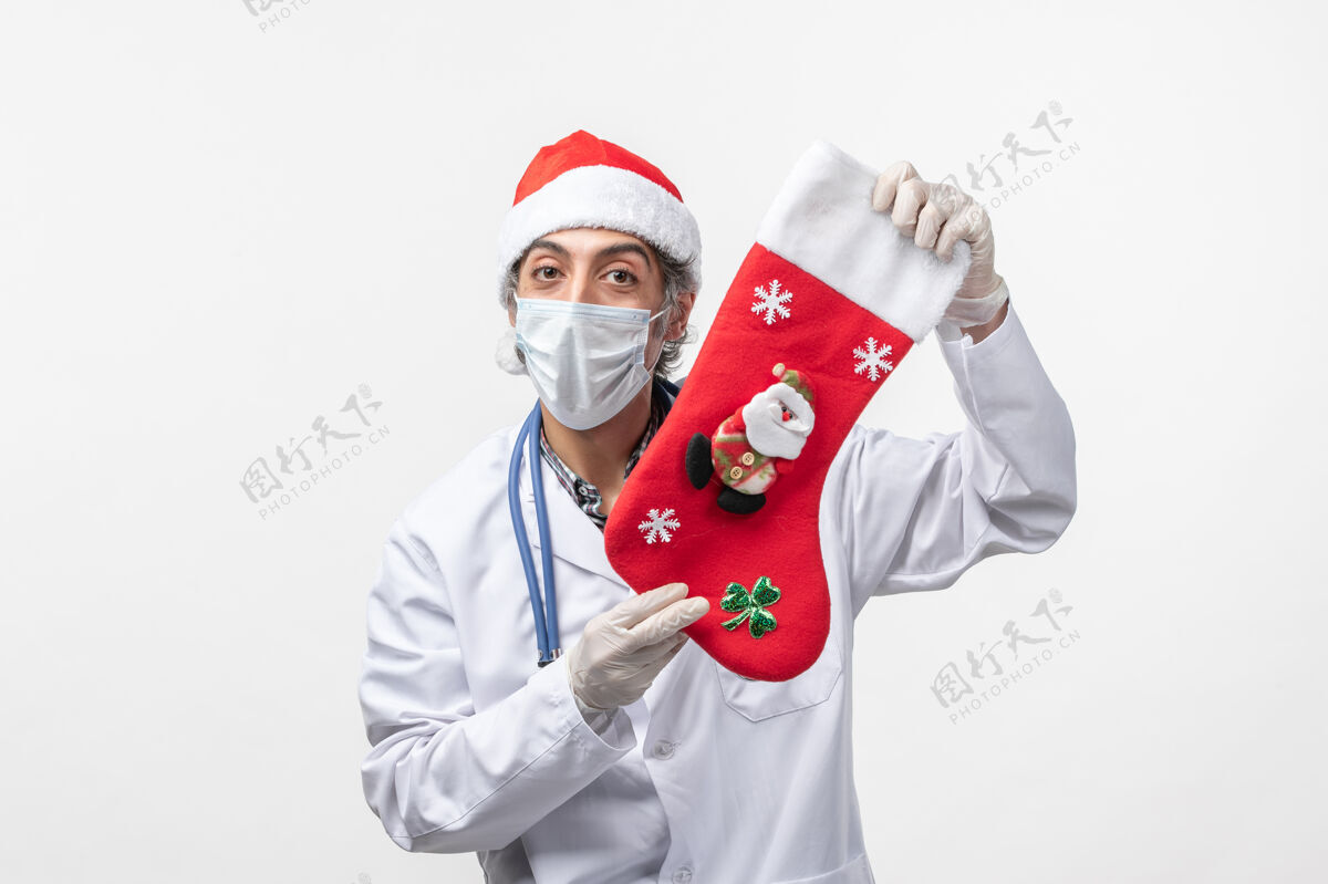 肖像正面图白色墙上戴着节日袜子的男医生-圣诞病毒病毒工作男医生