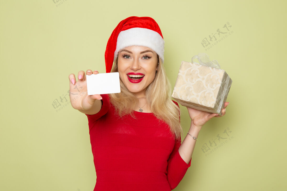 圣诞节前景靓女手持礼物和银行卡在绿色的墙上彩绘圣诞雪新年假期情感漂亮的女人情感肖像