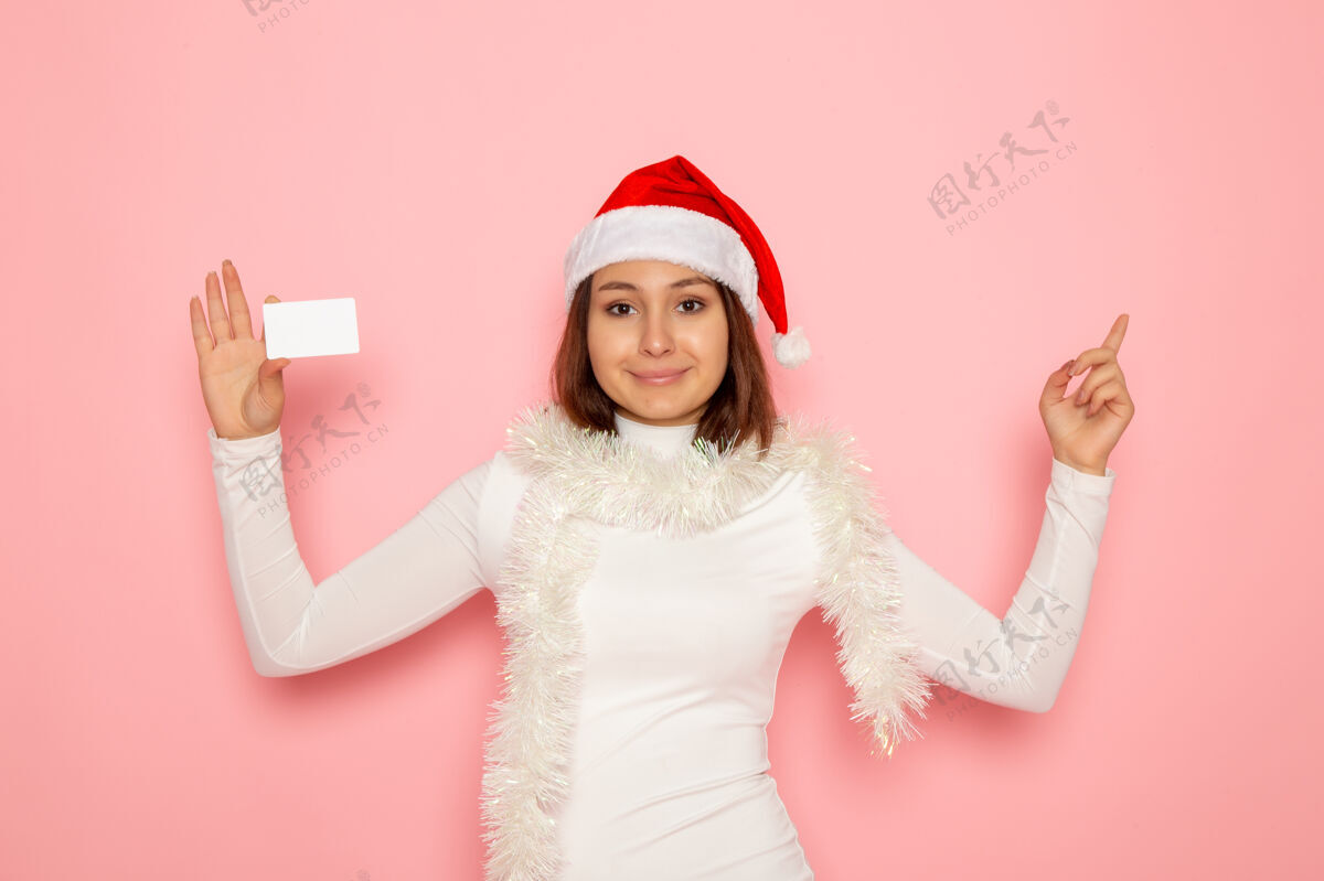 钱正面图年轻女性手持白色银行卡在粉色墙上圣诞新年时尚彩金假日颜色圣诞节漂亮