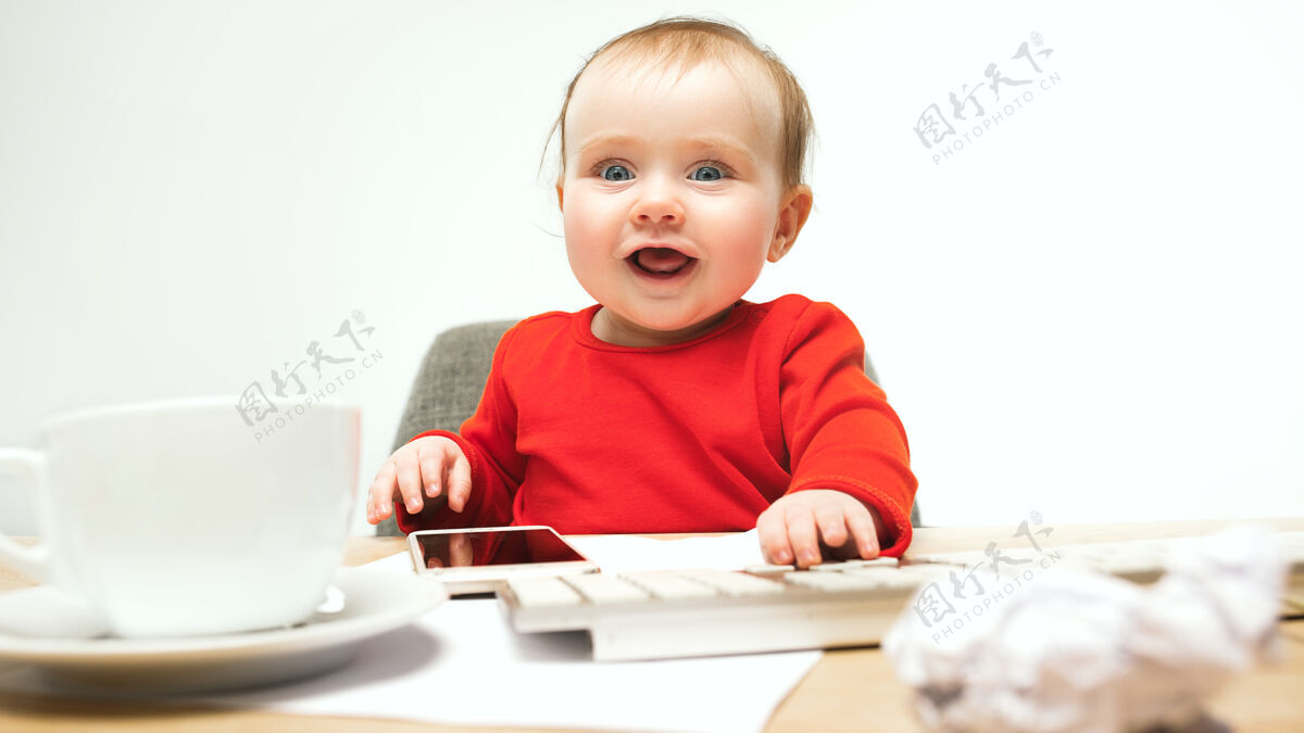 教育小女婴坐在白色工作室里 用现代电脑或笔记本电脑的键盘可爱婴儿年轻
