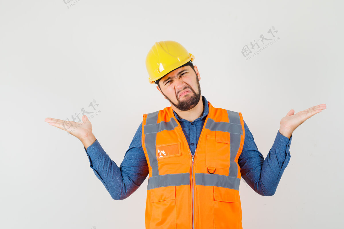 项目年轻的建设者在衬衫 背心 头盔前视图中做着比例尺的手势工作专业人