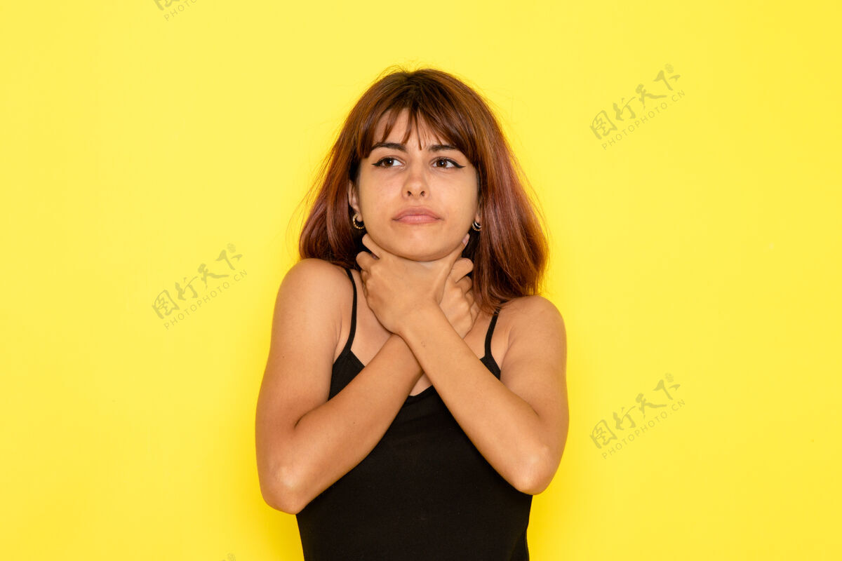 女孩身穿黑色衬衫和灰色牛仔裤的年轻女性在黄色墙壁上挤满了自己的前视图情感姿势前面