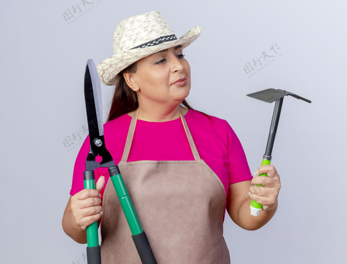 园丁穿着围裙 戴着帽子 拿着铲子和树篱修剪器的中年园丁们正困惑地看着他们站在白色的背景下做着选择帽子树篱白色
