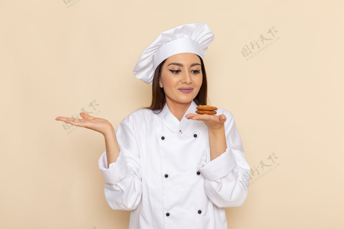 微笑身穿白色厨师服的年轻女厨师正拿着小饼干站在白墙上烹饪护士套装