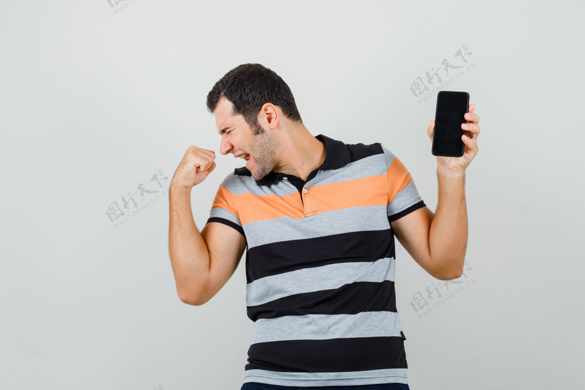 现代一个年轻人拿着手机 穿着t恤展示获奖者的姿态 看上去精力充沛而赢家展示