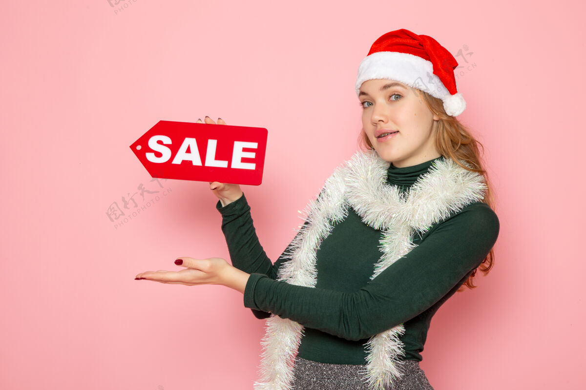 成人正面图年轻女子手持红色大甩卖在粉色墙上写圣诞假期新年照片购物时尚感慨风景写作购物