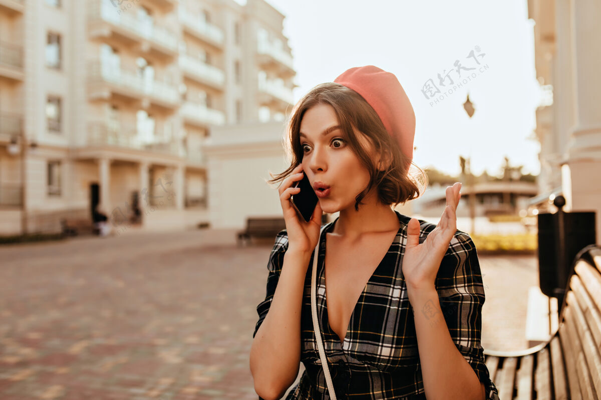 贝雷帽一个穿着优雅服装的年轻女子在电话里讲话 一张站在街上的法国女模特的户外画像情感红色贝雷帽时尚