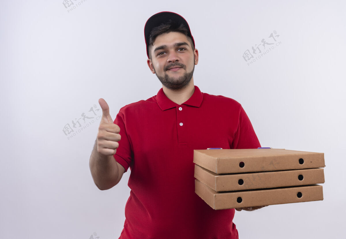 制服年轻的送货员身穿红色制服 头戴鸭舌帽 手里拿着一叠披萨盒 看上去自信地微笑着 竖起大拇指大拇指抱着展示