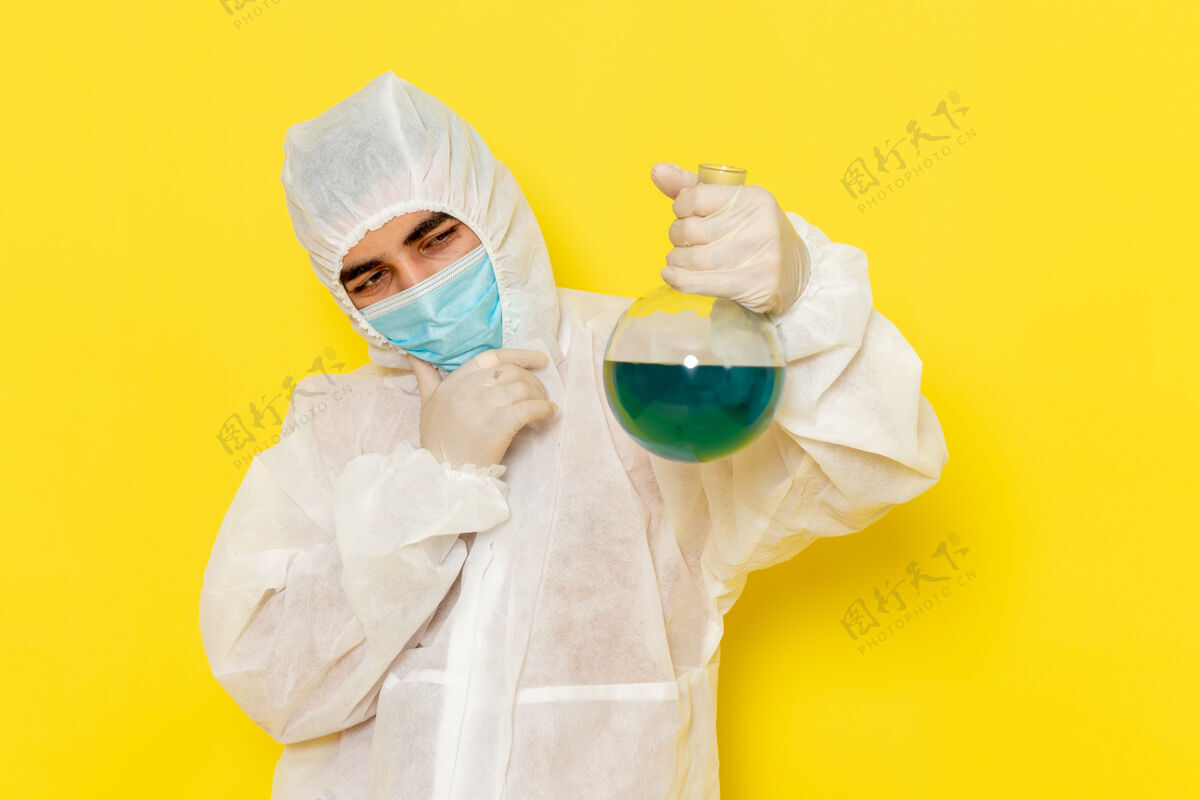 正面穿着特殊防护服的男科学工作者的正面图 戴着面具 拿着烧瓶 在黄色的墙上思考护士思维科学