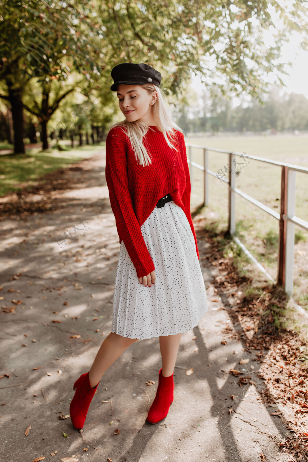 享受漂亮的金发女郎穿着时髦的红色毛衣和时髦的连衣裙 戴着黑色漂亮的帽子美丽的模特自信地在落叶中摆姿势浪漫秋天金发