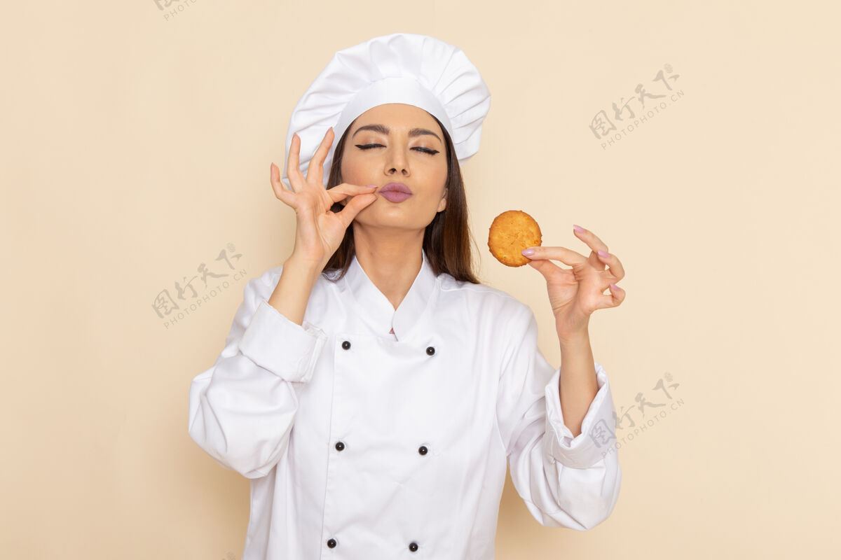 专业身穿白色厨师服的年轻女厨师正拿着糖饼干站在浅白的墙上食物肖像成人