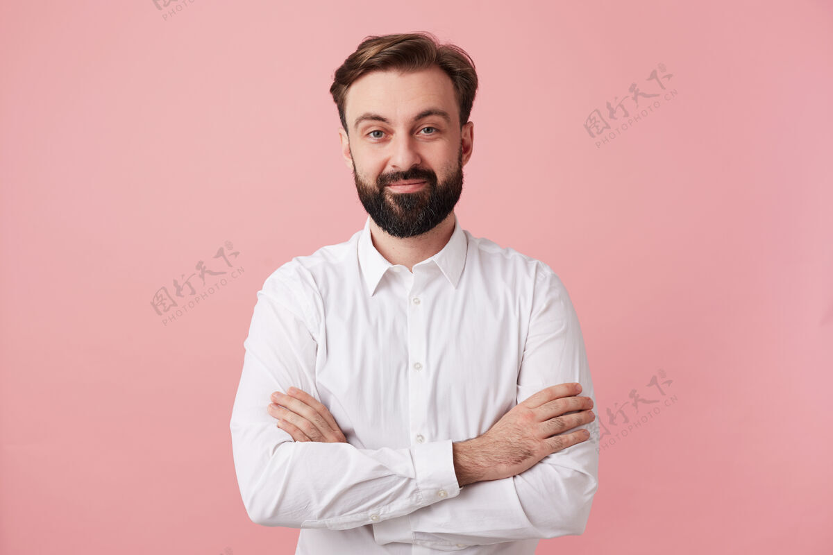 胡须年轻漂亮的黑发男性 留着胡须 面带迷人的正面微笑 穿着正式的衣服 双手合十地站在粉红色的墙上成人男子气概手