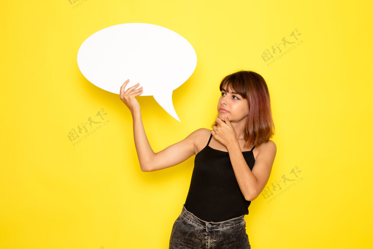 前面身穿黑色衬衫的年轻女性正拿着一个白色的大牌子 在淡黄色的墙上思考情绪漂亮衬衫
