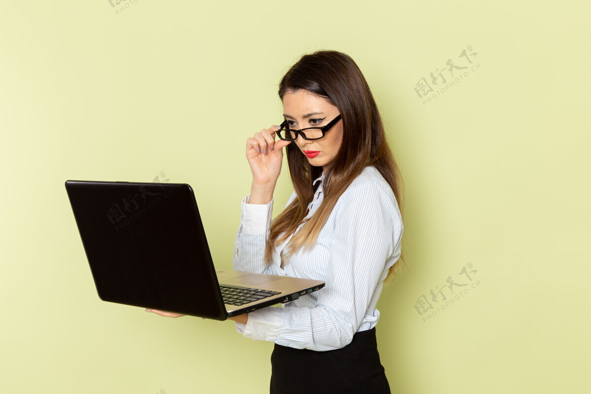 灯光穿着白衬衫和黑裙子的女上班族在浅绿色墙上拿着笔记本电脑的正视图笔记本电脑工作衬衫