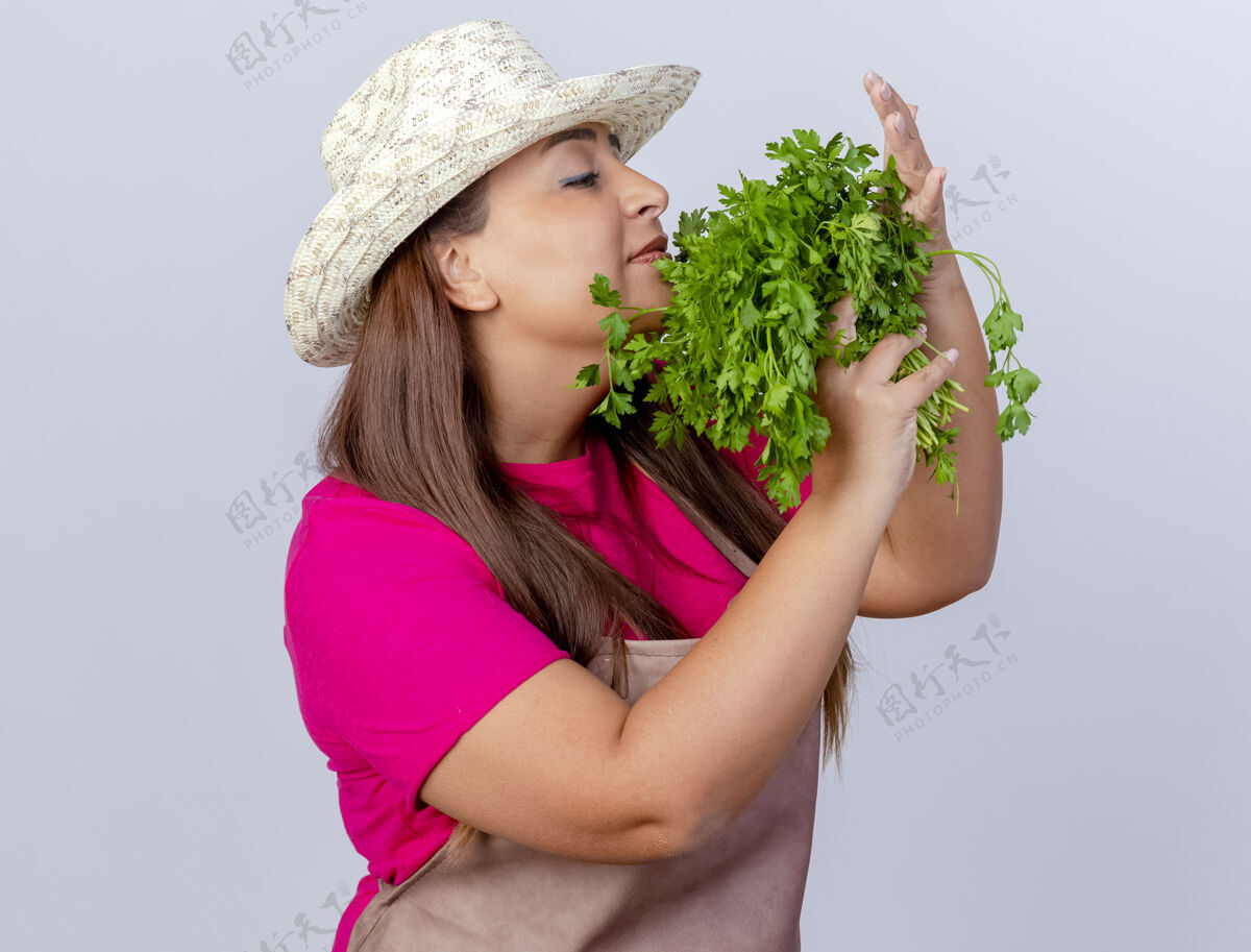香气围裙戴帽子的中年园丁妇女站在白色的背景上 手里拿着新鲜的香草 散发着芳香中期草药女人