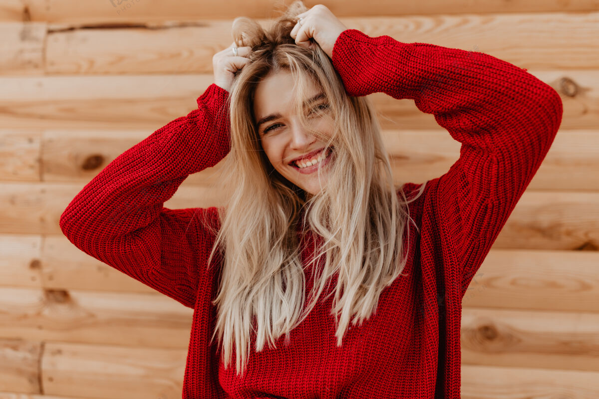 快乐一个漂亮的金发女郎在木墙上快乐地微笑的特写照片穿着红色毛衣的漂亮女孩在户外感到快乐放松户外肖像