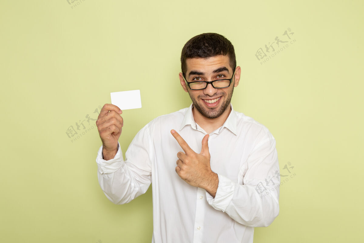 前面身穿白衬衫 手持白色塑料卡的男性上班族在浅绿色墙上的正面照片实验室外套工人医疗