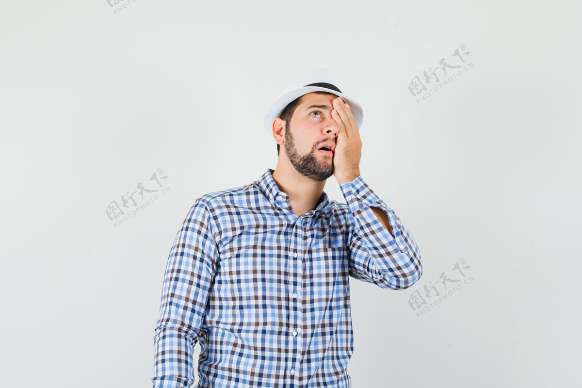 人类穿着格子衬衫 戴着帽子 手放在眼睛上的年轻男子抬起头来 神情焦急前视图手肖像发型