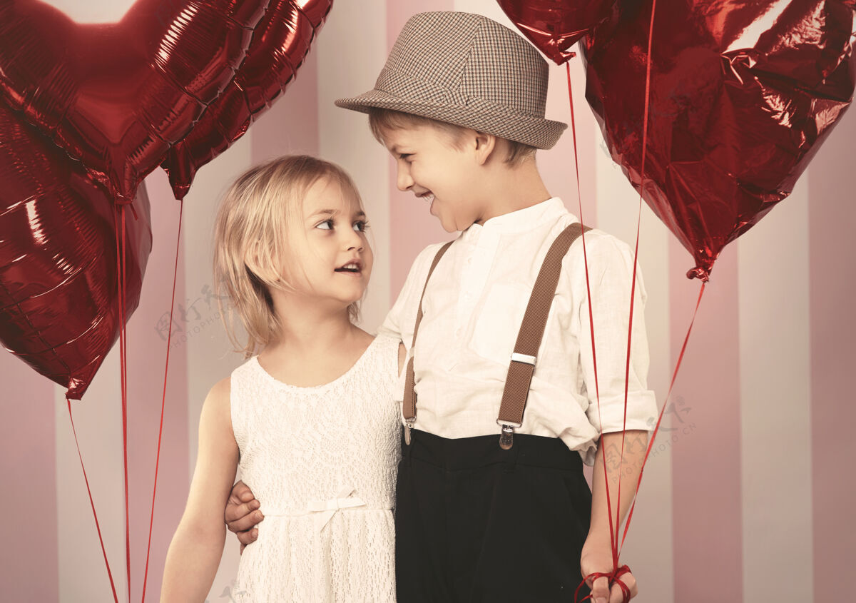 看两个相爱的孩子和气球站在一起站着帽子兴奋