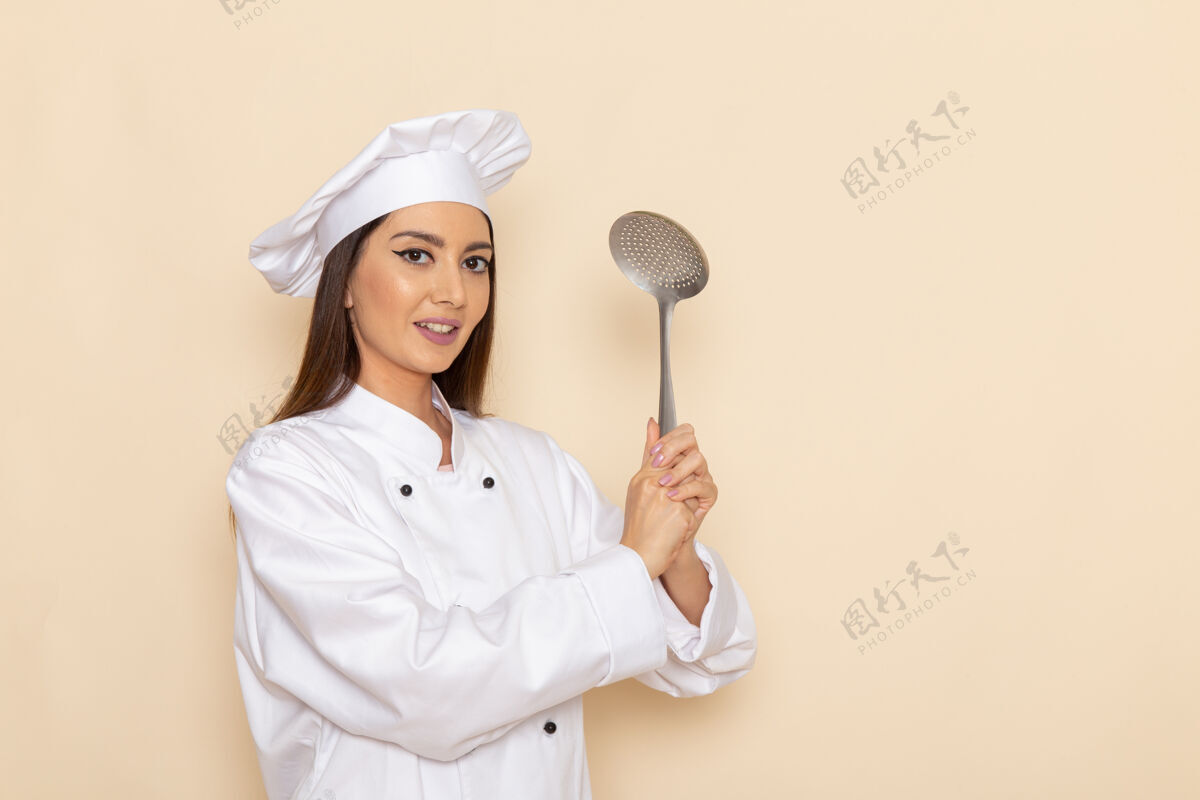 银身穿白色厨师服的年轻女厨师正拿着银色大勺子站在浅白的墙上厨房大烹饪