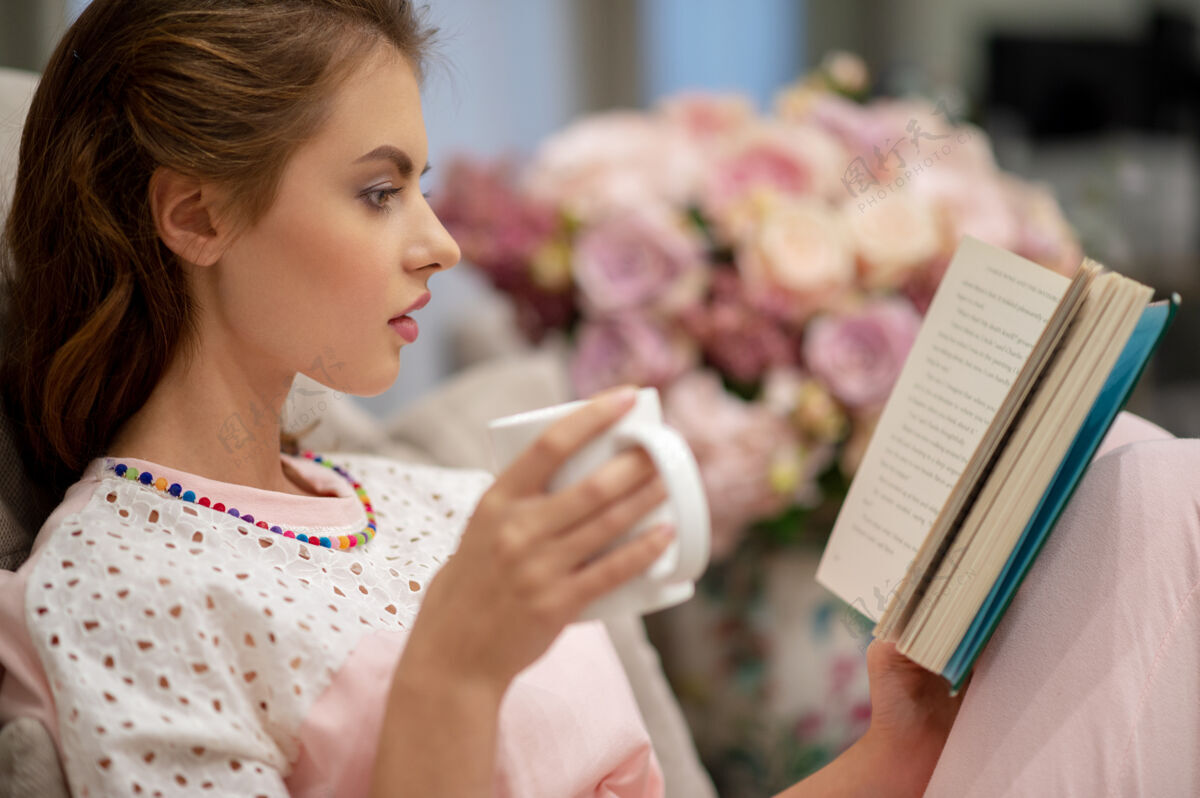 室内年轻漂亮的女人坐在沙发上喝着咖啡看书享受着休息咖啡成人年轻